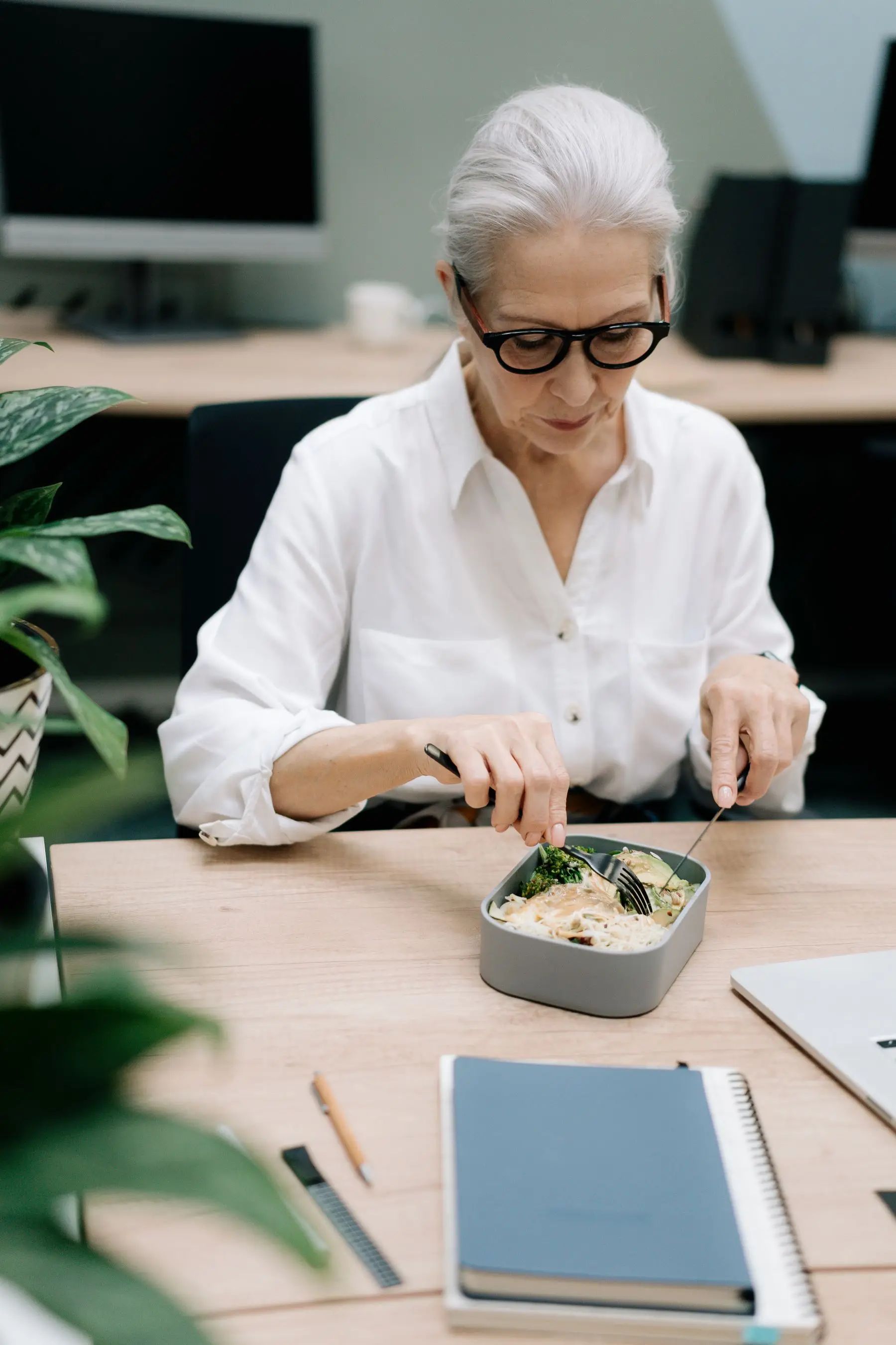 Frau isst ihr mitgebrachtes Mittagessen am Schreibtisch im Büro
